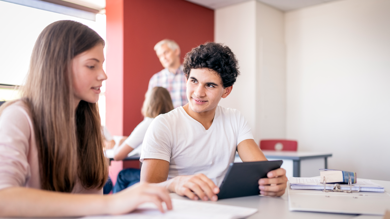 Teenage male and female student in a classroom using a tablet