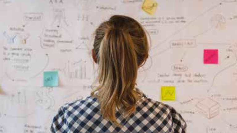 An image of a woman standing in front of a white board filled with sticky notes.