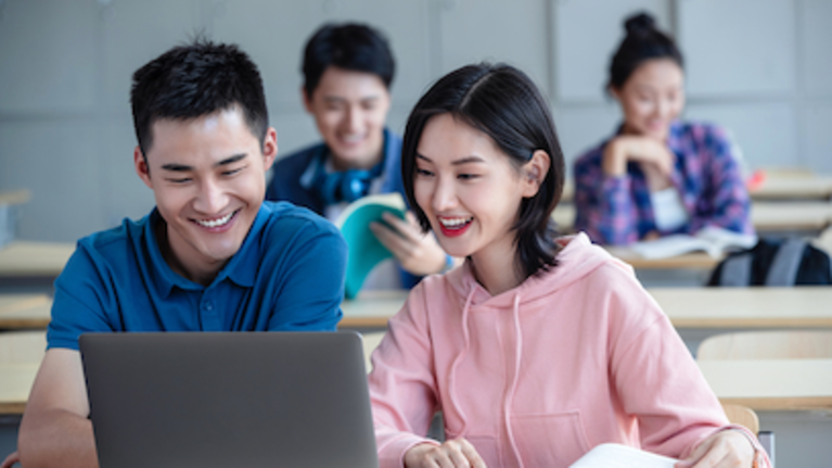 Two young people happily using a laptop together, smiling and engaged in their work.