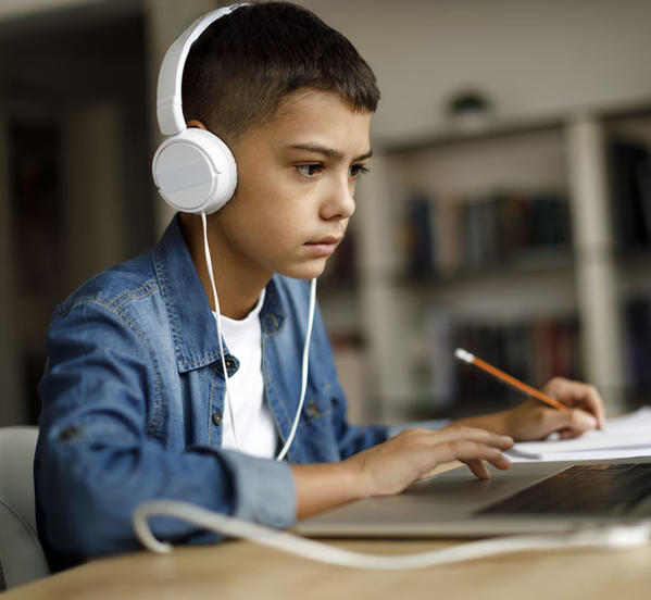 Young boy wearing headphones working on a laptop at home.