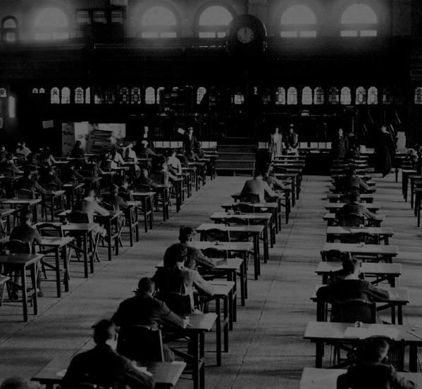 Historic photograph of an examination taking place in a large hall.