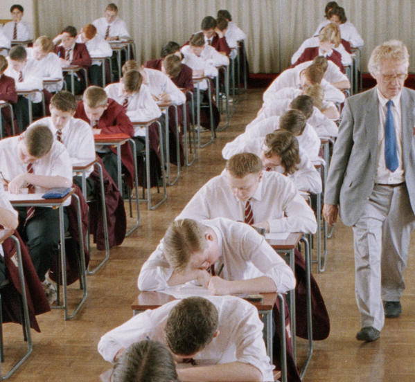 Pupils wearing school uniform sitting at exam tables in a school gymnasium.