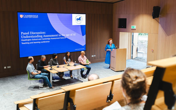 A panel of education experts sit around a table to address questions around AI and assessment to an audience of attendees inside the Hive Lecture Theatre at Headington School