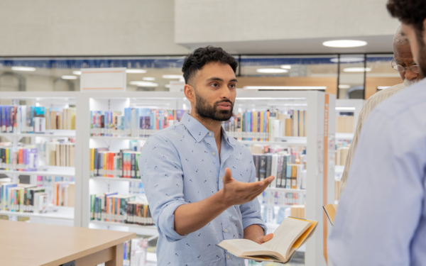 Three people discussing a book in a library setting.
