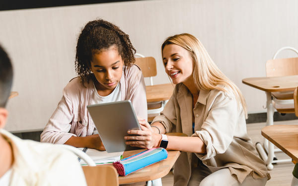 student and smiling teacher looking at an iPad device together in the classroom