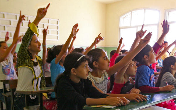 Students in a classroom with their hands raised up
