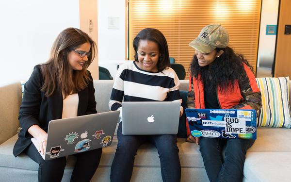 Three women sat on a sofa looking at their laptops