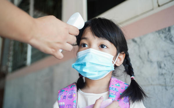 Teacher checks student temperature at preschool entrance, Thailand