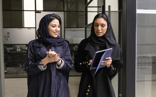Two colleagues talk to each other, one points at a tablet computer