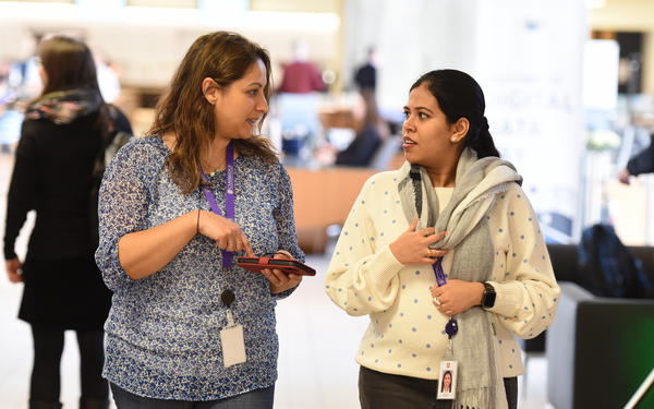 Two female colleagues look at each other in conversation while walking towards the camera