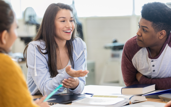 Teen girl smiles as she debates with peers in a classroom