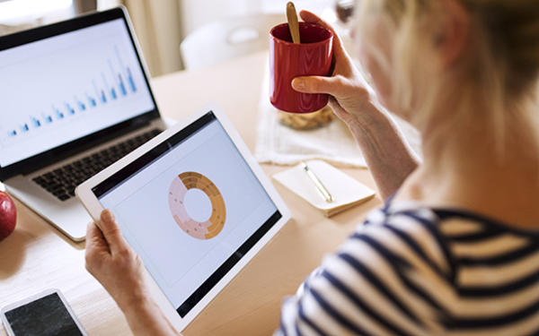 Woman looking at two different graphs on tablet and laptop screens