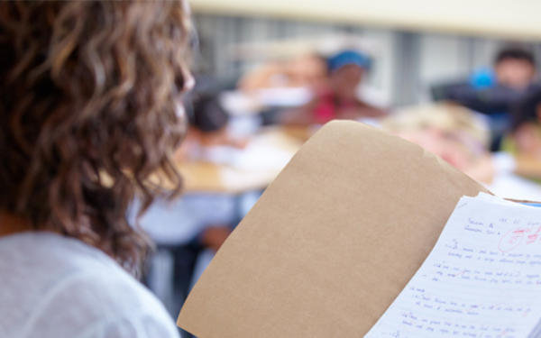 Teacher standing in a classroom looking at a graded paper