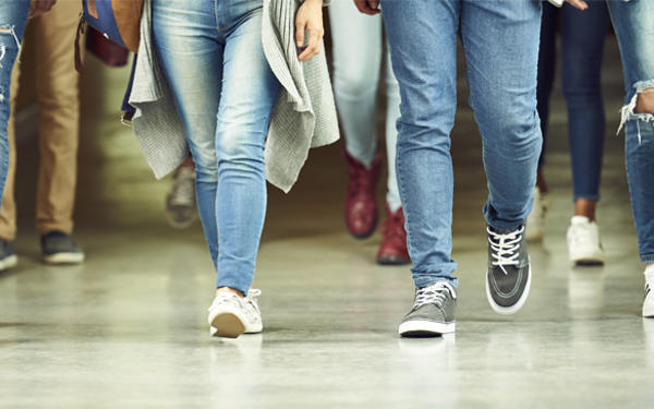 The legs of students walking forwards along a corridor