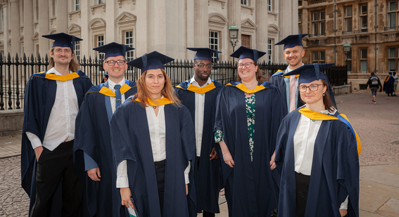 Cambridge's first-ever cohort of data scientist BSc graduates stand and pose outside the Old Schools building dressed in navy and yellow cap and gowns.