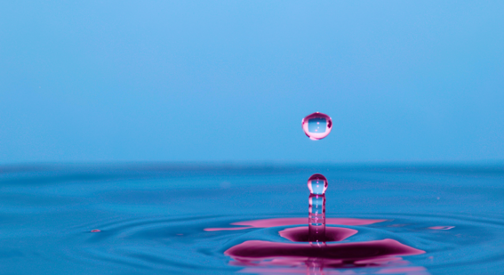 A vibrant image capturing a single droplet of water in mid-air with a serene blue background, creating a ripple on the water surface below.