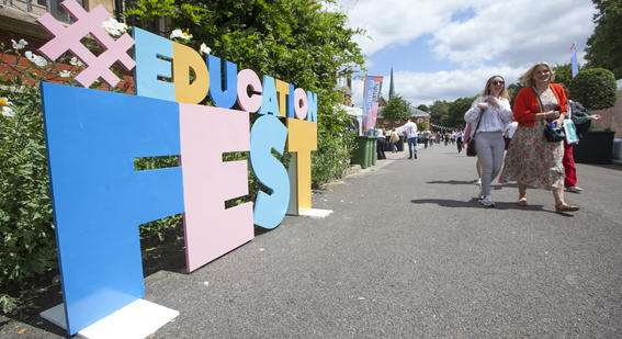large letter standing on the ground spelling out the phrase hashtag education fest with two smiling festival goers are walking past