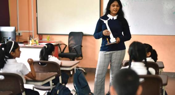 Teacher standing in front of classroom holding model wind turbine