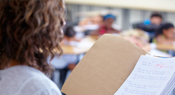 Teacher standing in a classroom looking at a graded paper