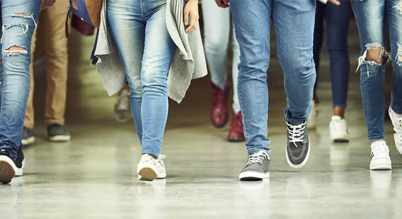 The legs of students walking forwards along a corridor